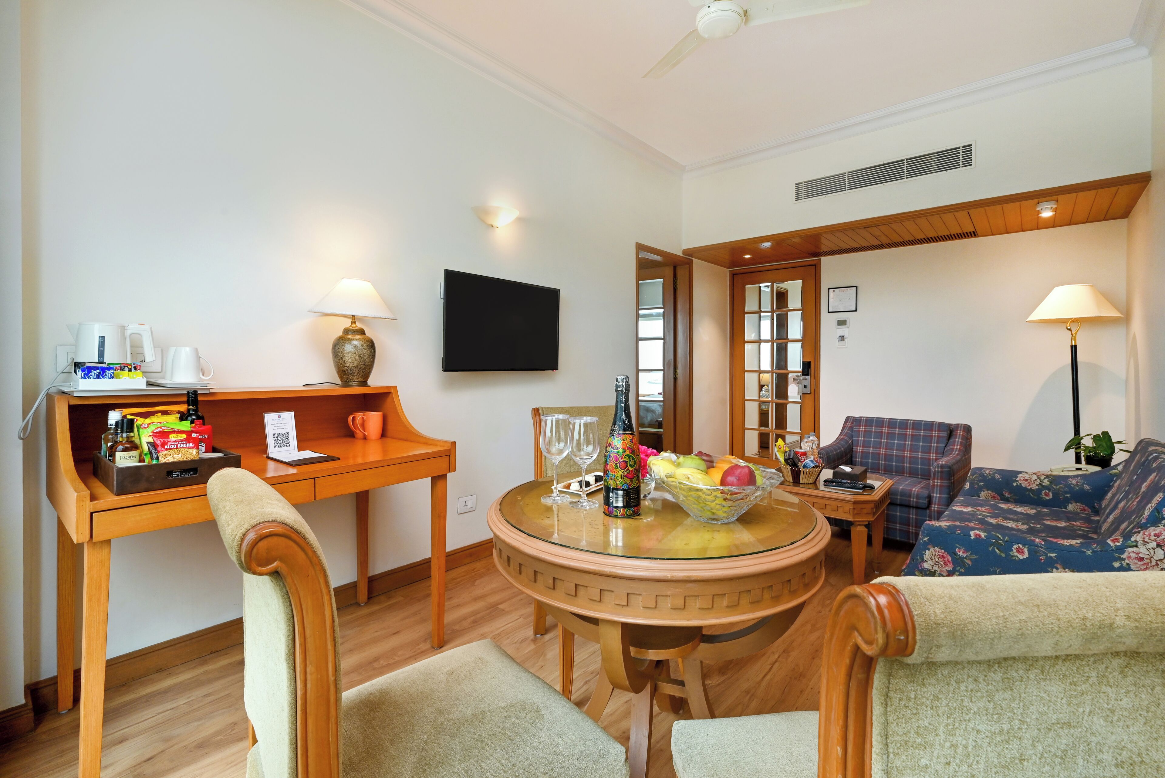 A living room with a round glass table, wooden chairs, a sofa, a television, and a coffee station.