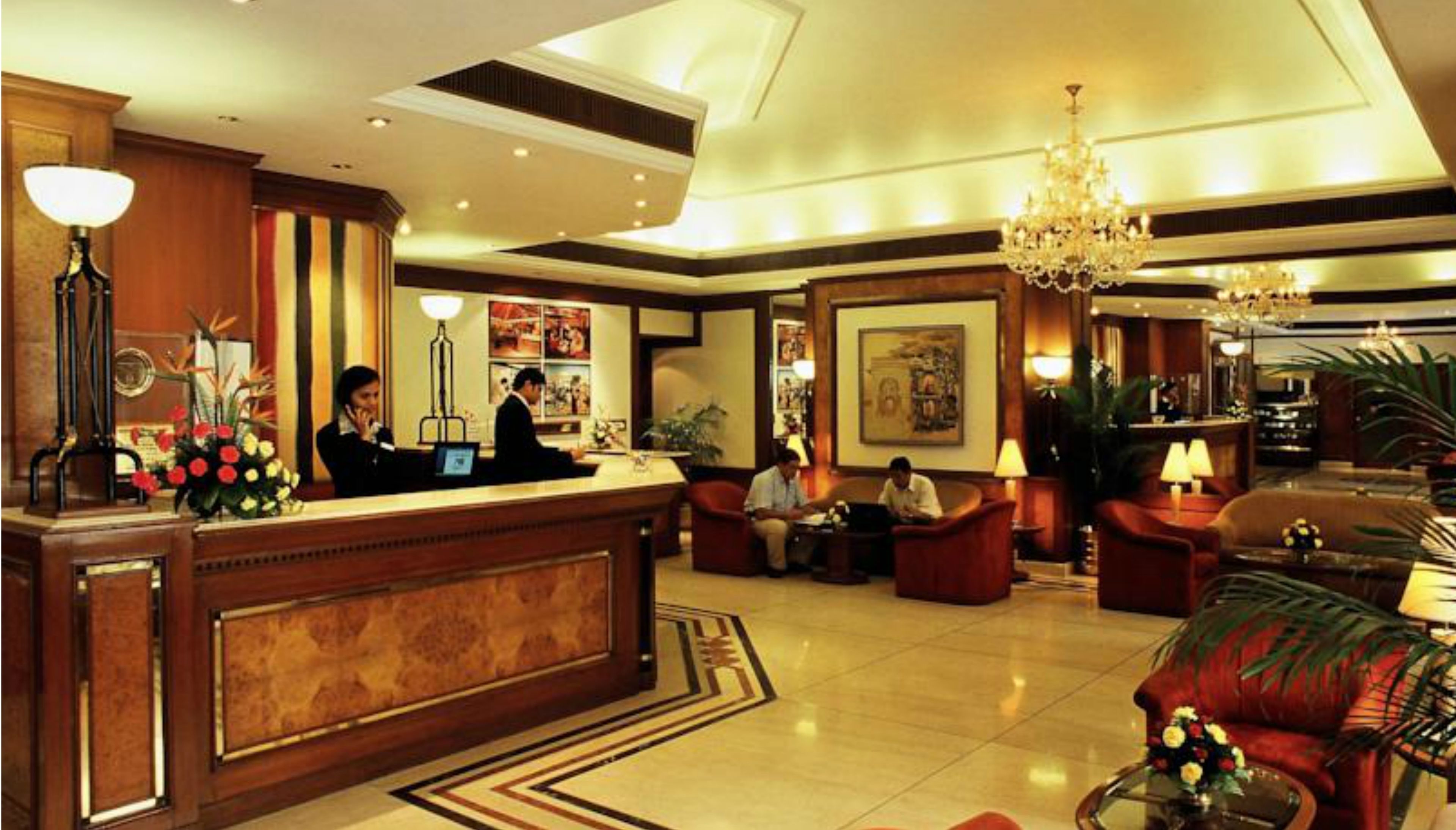 Un vestíbulo de hotel con mostrador de recepción, zonas de estar y una araña.