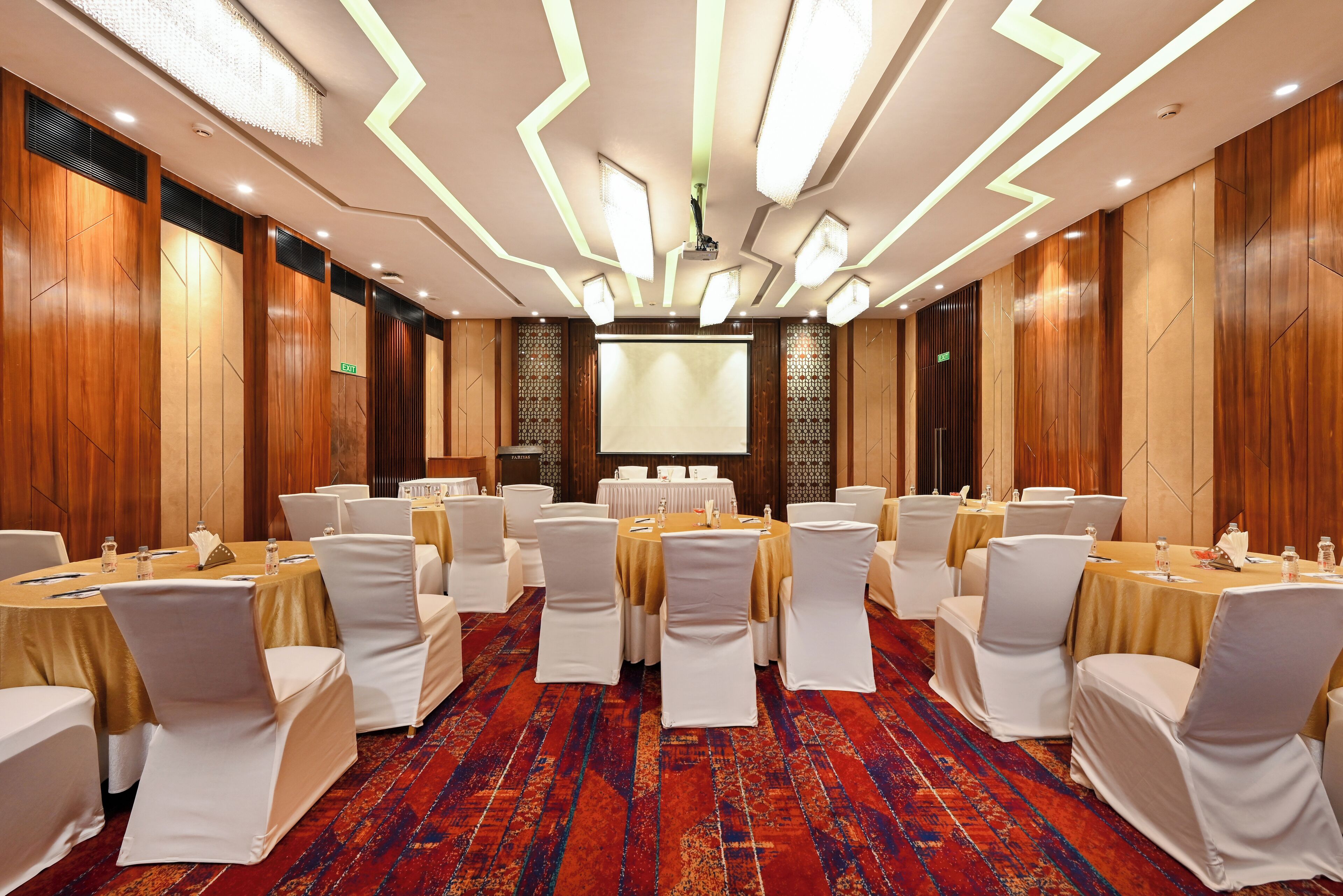 A conference room with round tables, white chairs, and a large screen at the front.