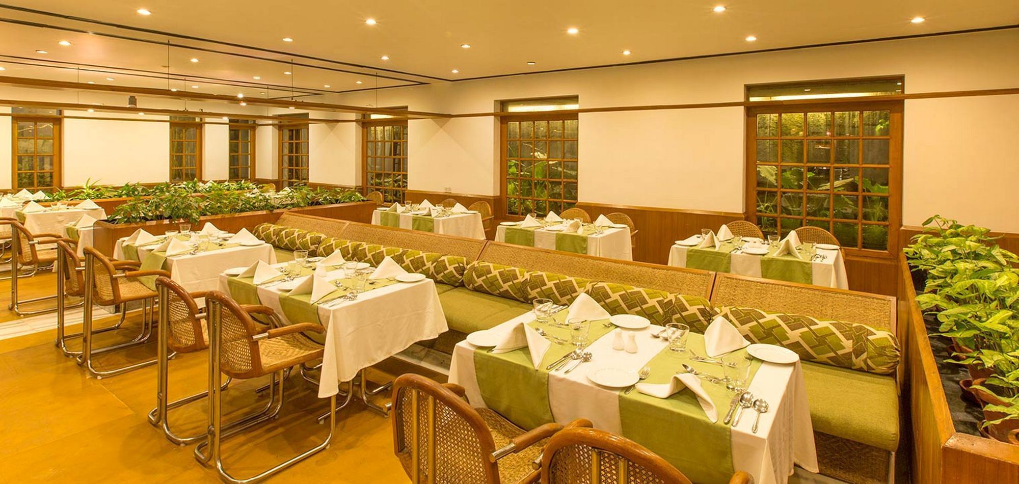 Un espace repas avec plusieurs tables dressées pour les convives, agrémenté de nappes vertes et de serviettes blanches.