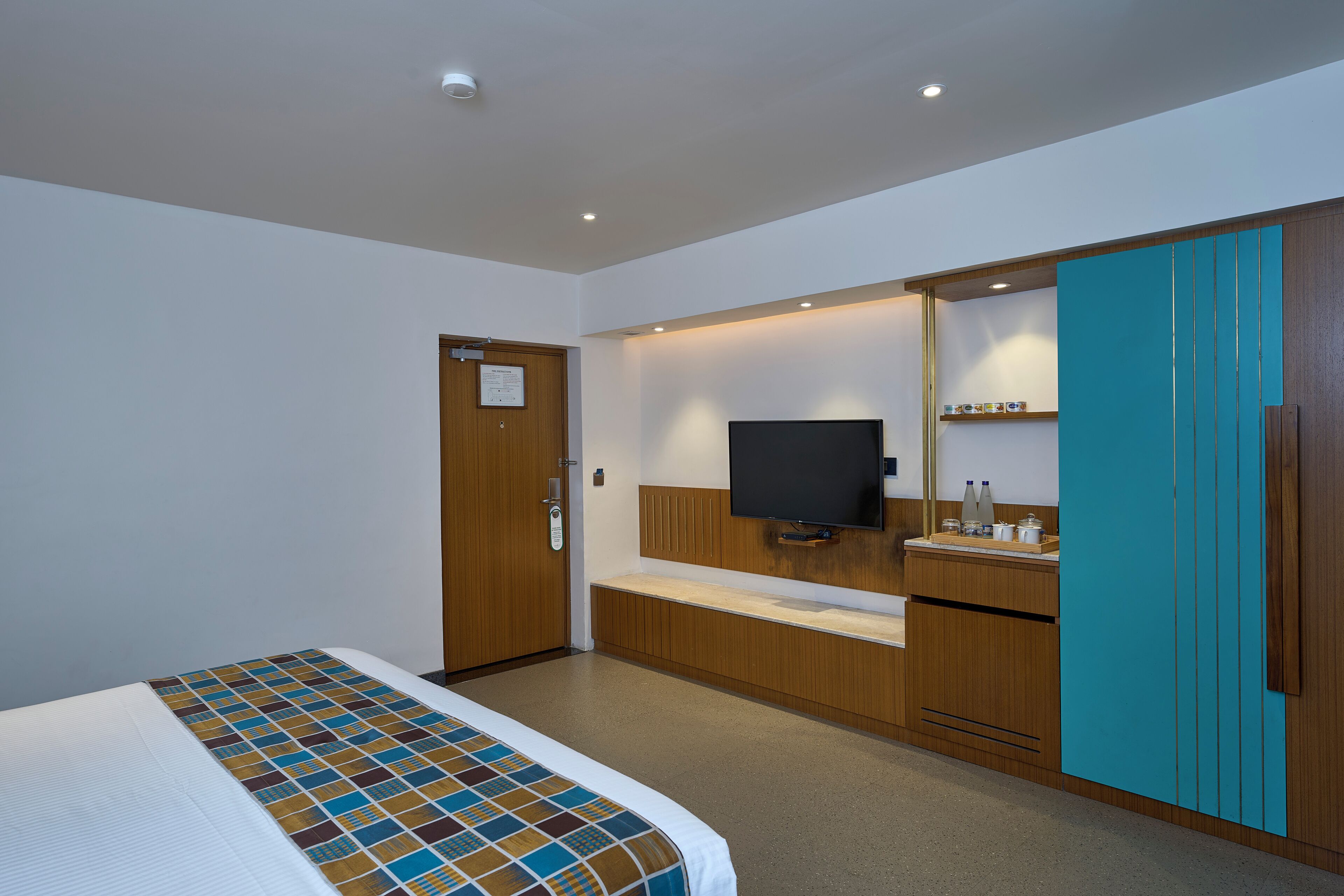 A hotel room with a bed, a television, a wooden wardrobe, and a small shelf with toiletries.