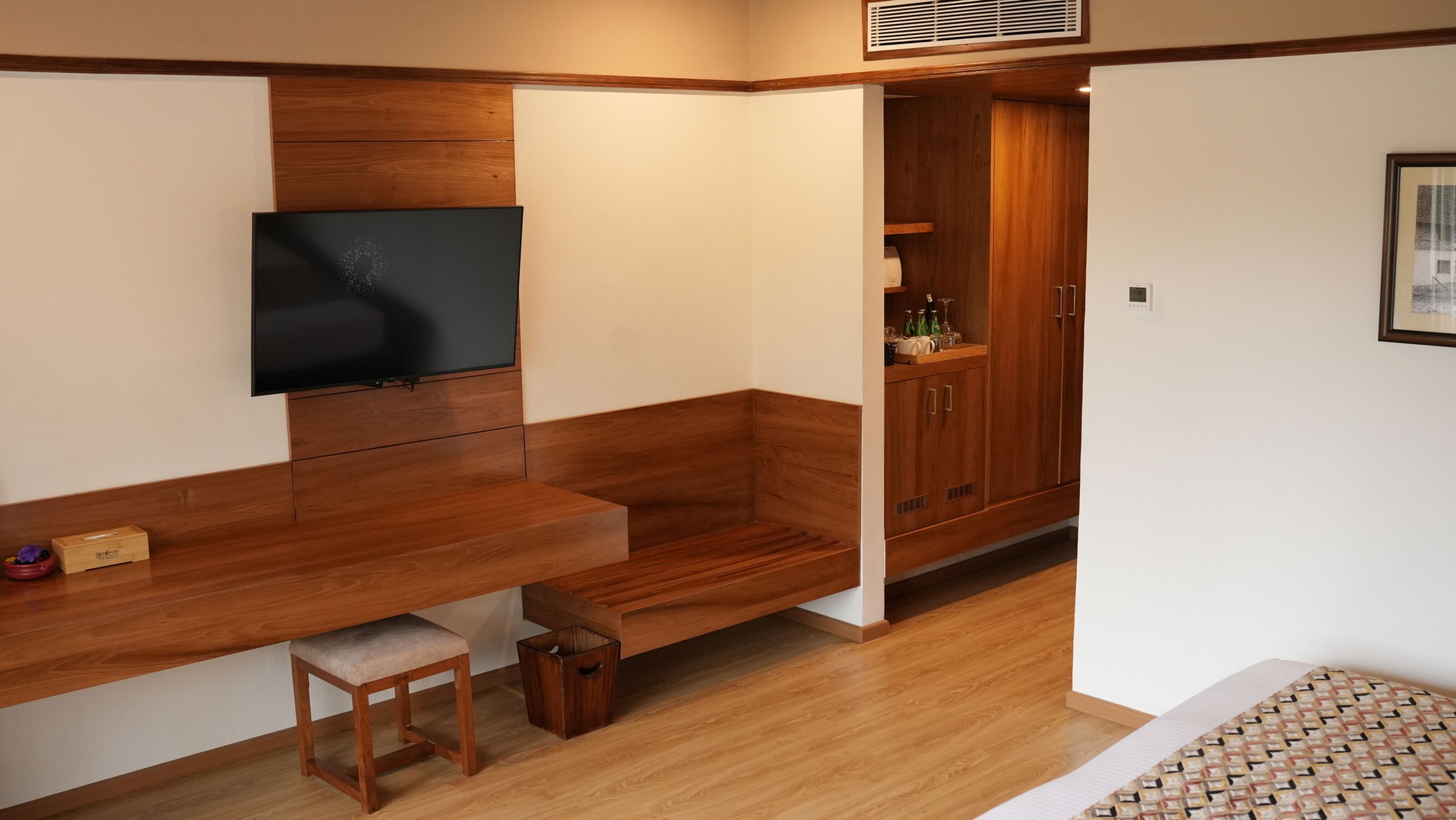 Un espacio habitable reducido con un banco de madera, un televisor, un taburete pequeño y un mueble con botellas.