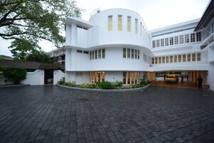 Um edifício moderno com fachada curva, várias janelas e um pátio pavimentado.