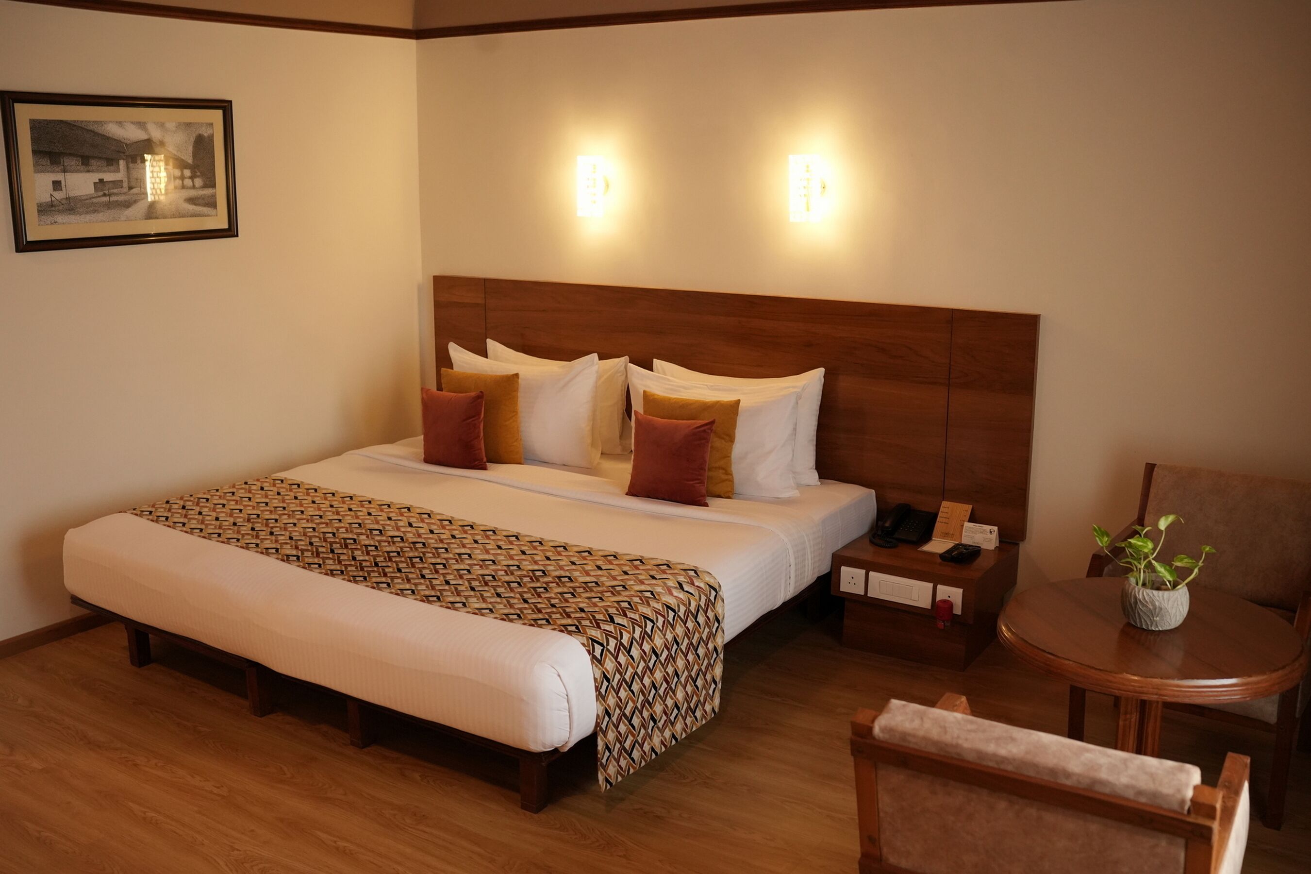 A hotel room with a large bed, bedside tables, a chair, and a small table with a plant.