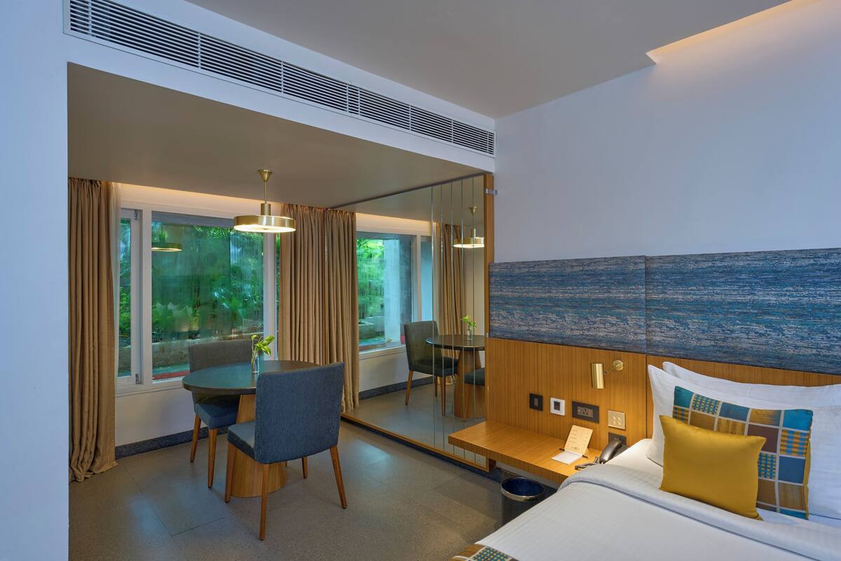 Una habitación de hotel con cama, mesita de noche, lámpara, sillón y una mesa de comedor con sillas.