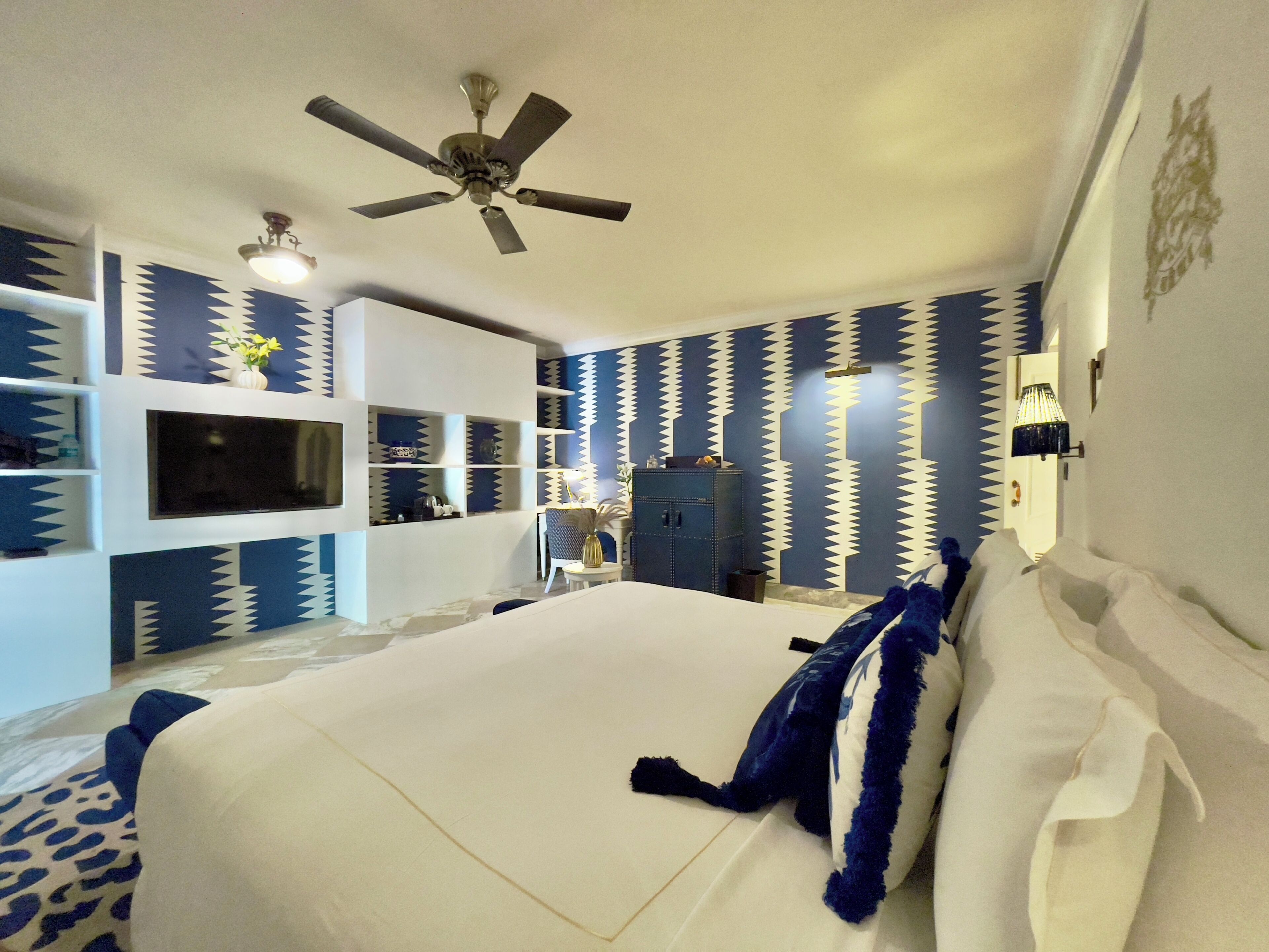 A bedroom with a bed, a ceiling fan, built-in shelves, a TV, and a wardrobe.