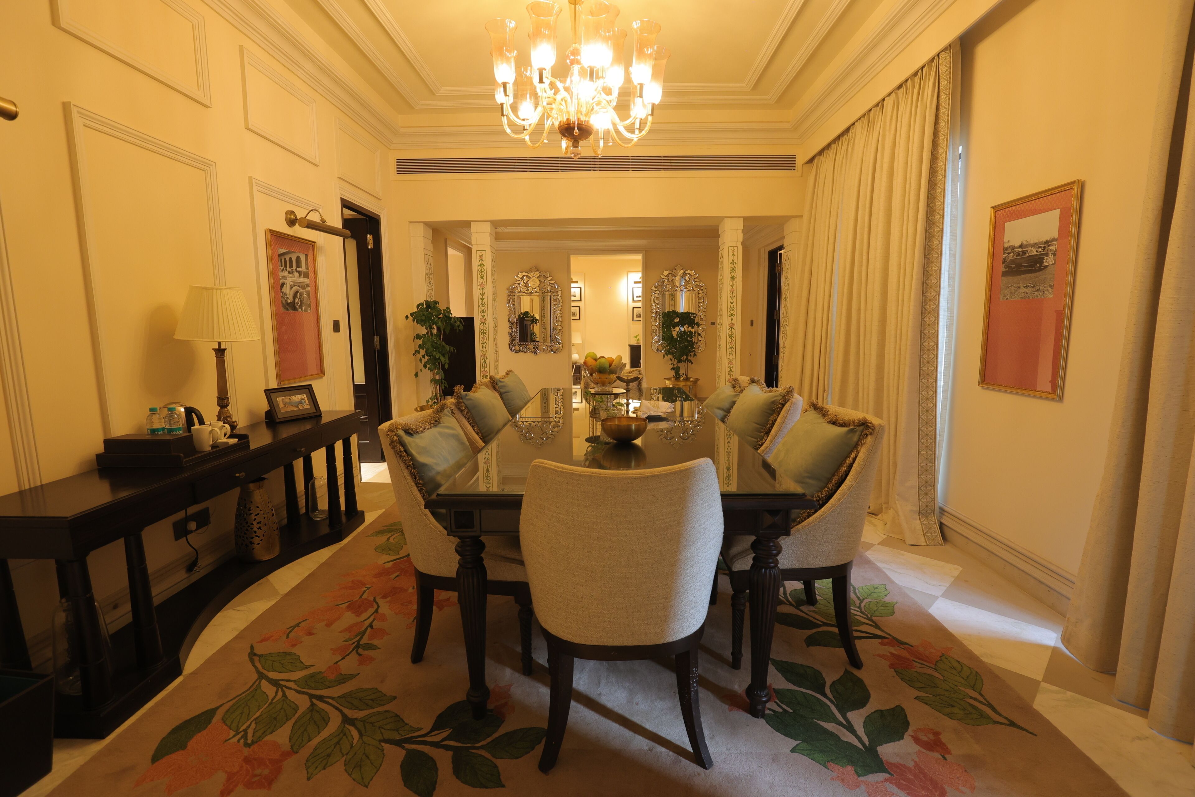 A formal dining room with a chandelier, a floral carpet, and a dining table set for six.