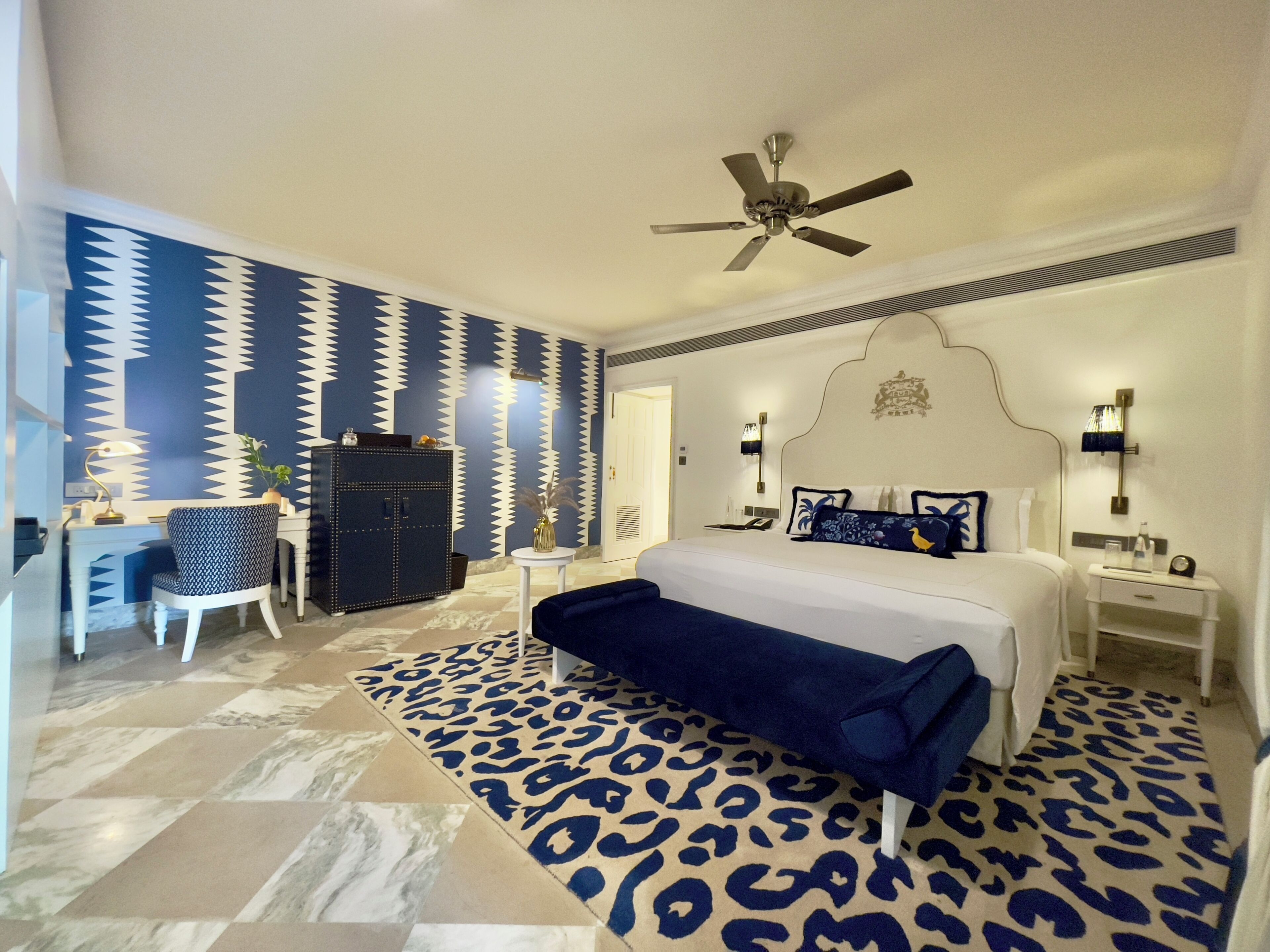 A bedroom with a bed, a desk, a chair, a wardrobe, and a ceiling fan.