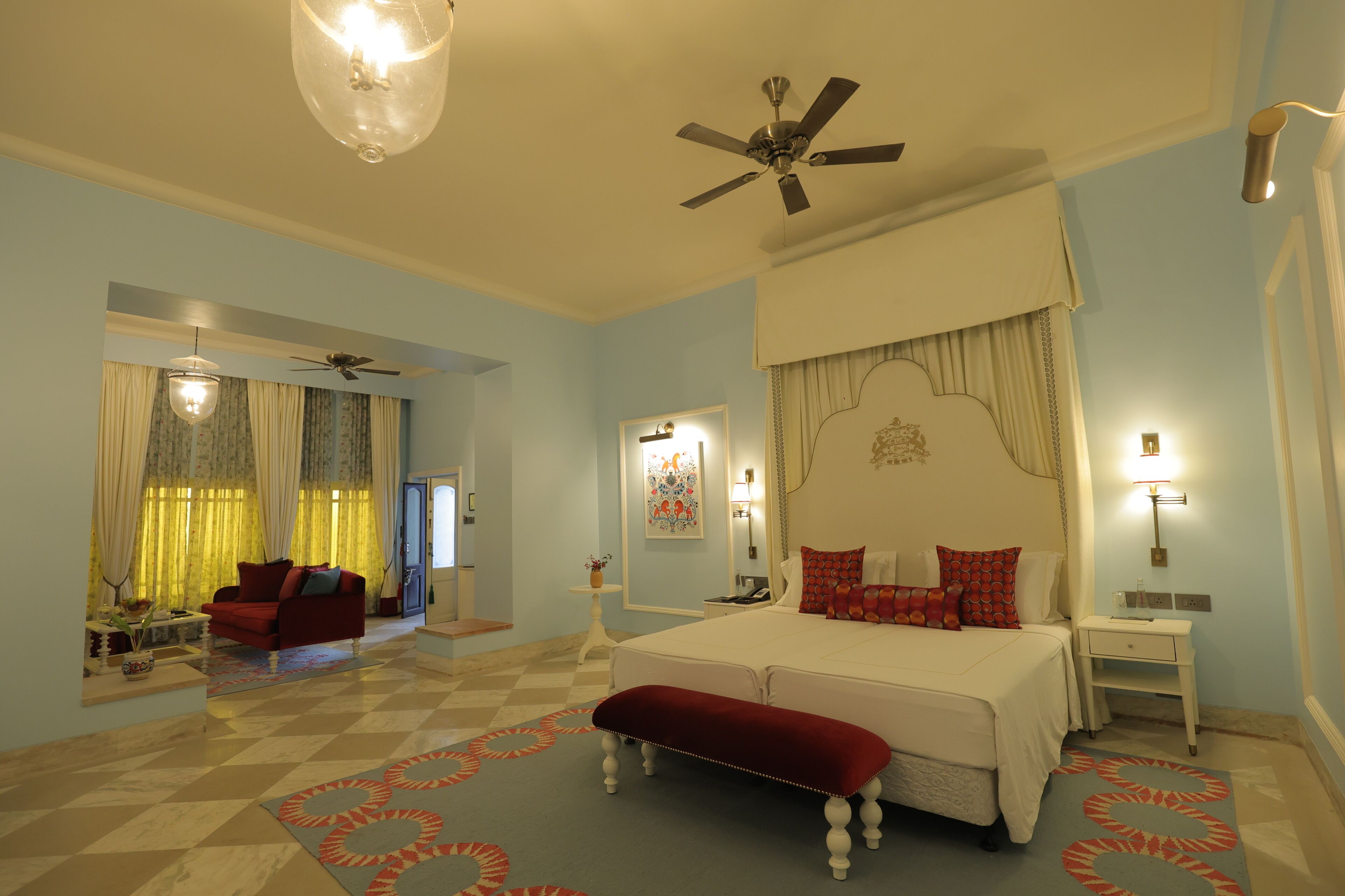 A bedroom with a large bed, a ceiling fan, a red bench, and a checkered floor.