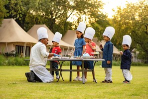 A group of people in chef hats gathered around a table outdoors with tents in the background.