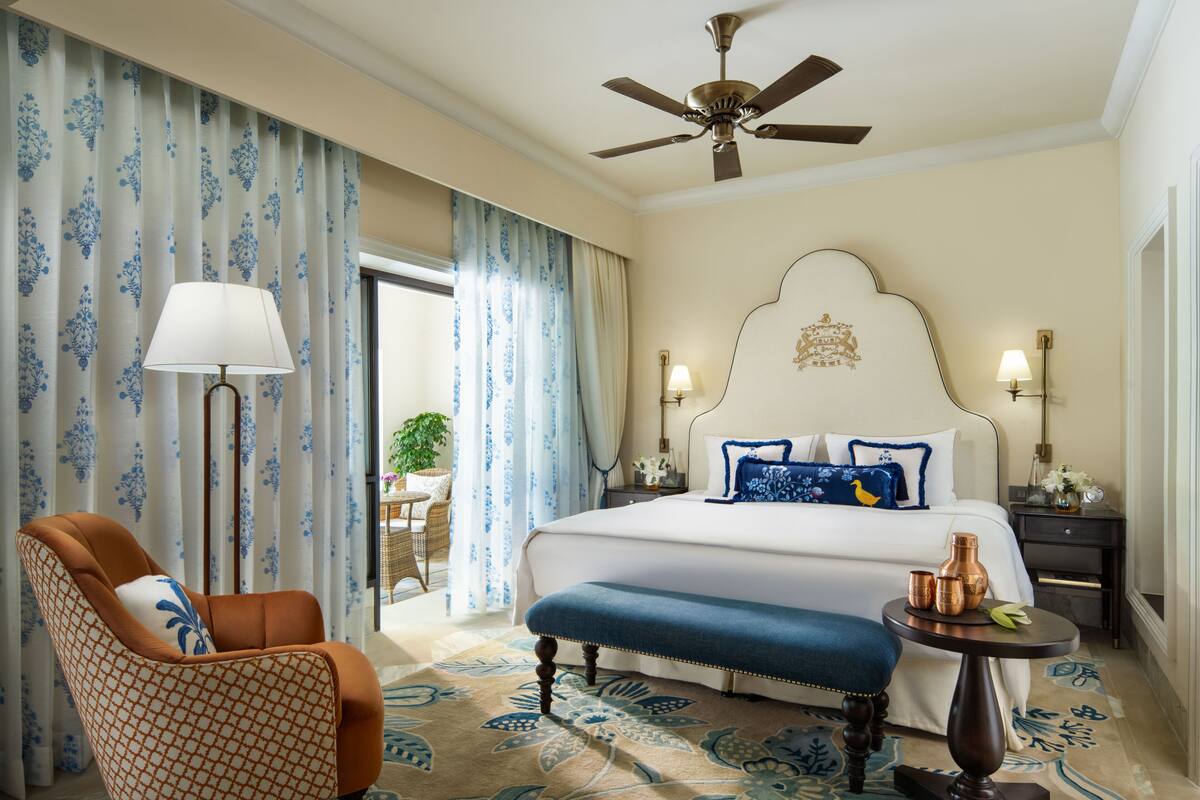 Une chambre d’hôtel avec un grand lit, un ventilateur de plafond, une chaise, une table avec une lampe et une vue sur l’extérieur.