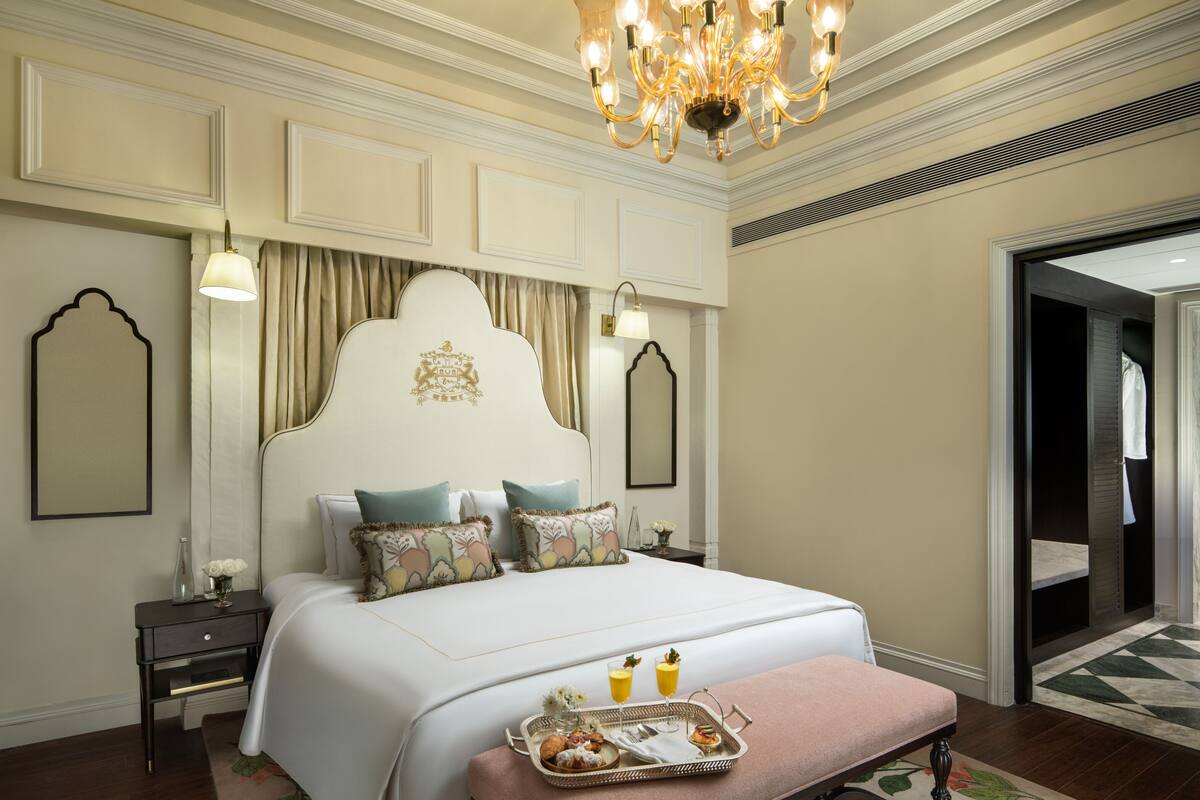 Une chambre spacieuse avec un grand lit, un lustre, une table de chevet et un plateau contenant des articles pour le petit-déjeuner.