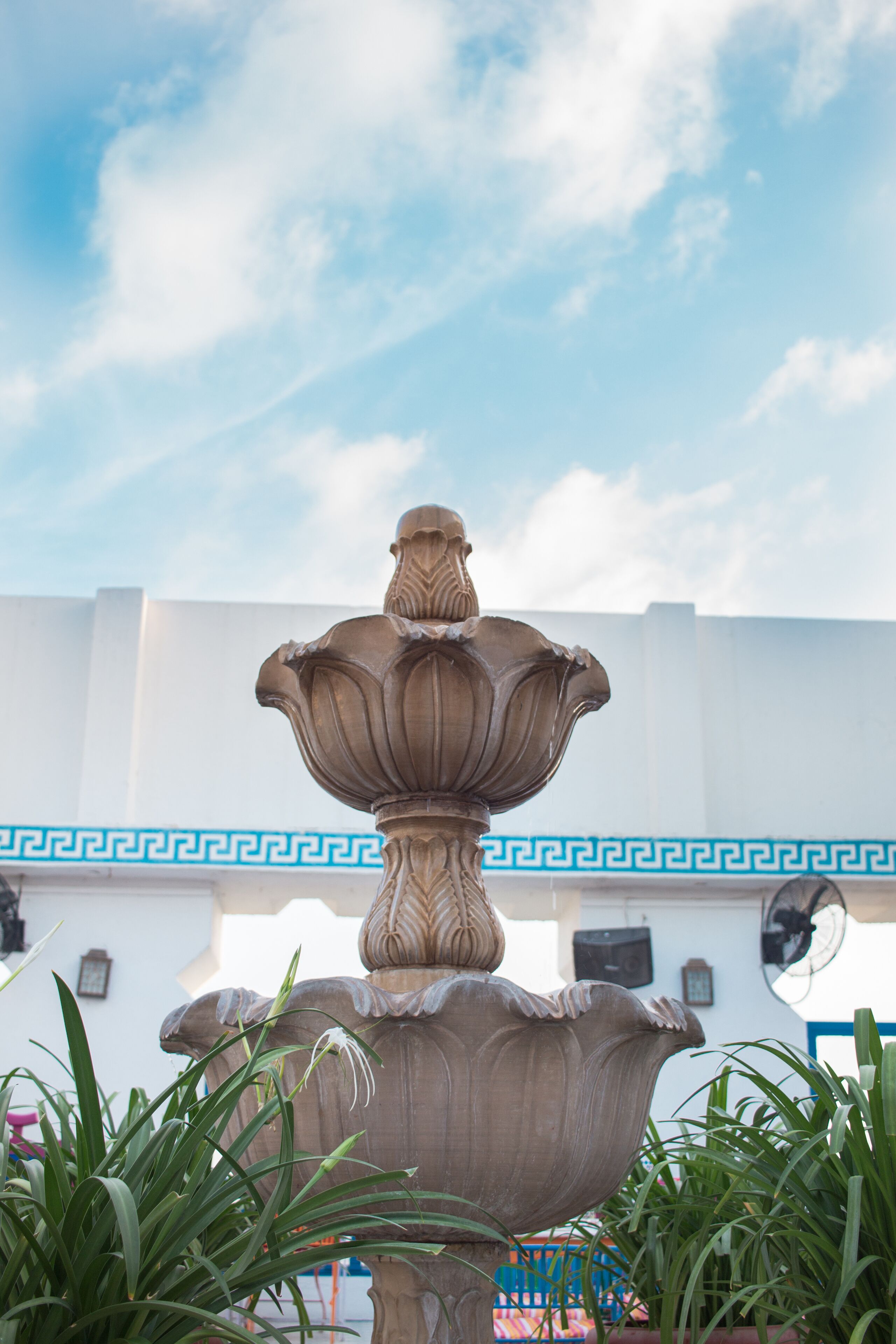 A stone fountain with a decorative top, surrounded by green plants.