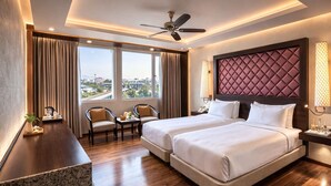 A hotel room with a large bed, two bedside tables, a desk, two chairs, a ceiling fan, and a city view. - Clarks Avadh, Lucknow (Lucknow)