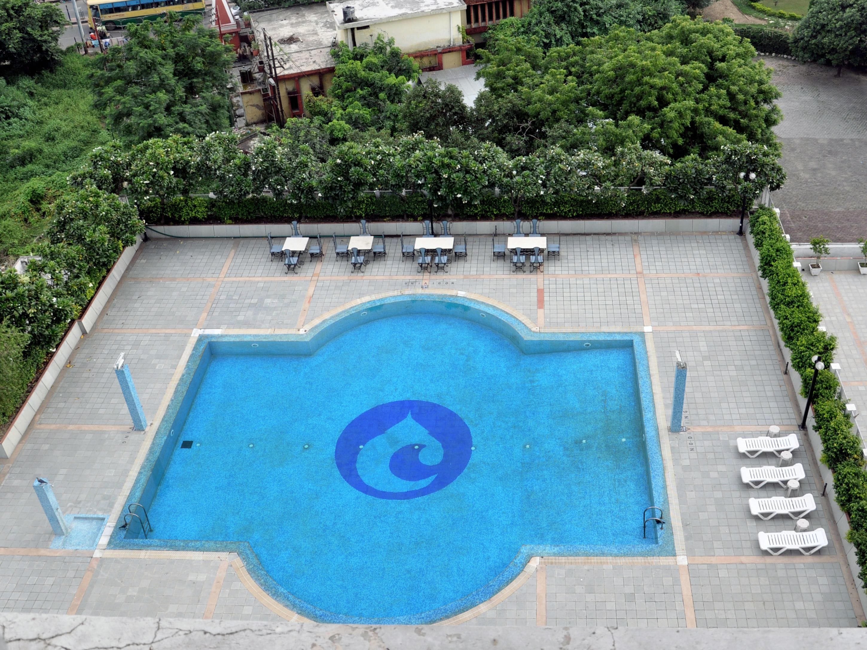 Une piscine avec un logo bleu, entourée de chaises longues et bordée d’une terrasse dallée.