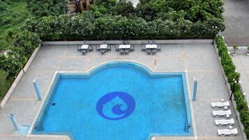 A swimming pool with a blue logo, surrounded by lounge chairs and a paved deck.