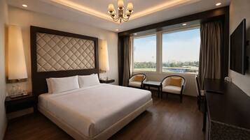 Habitación de hotel con una cama grande, dos sillas, un escritorio, un televisor y una ventana con vista a la ciudad.
