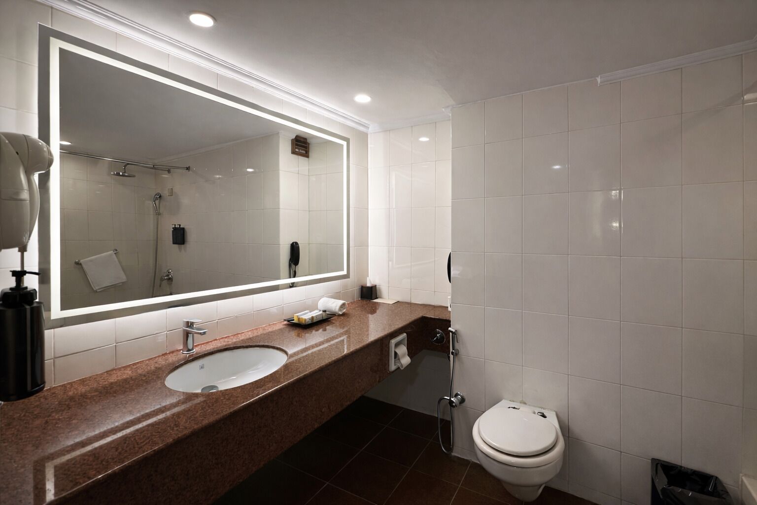 A modern bathroom with a large mirror, a sink, a toilet, and a shower.