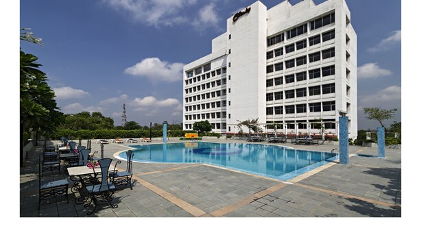 A modern hotel with a swimming pool, outdoor seating, and a large building in the background.