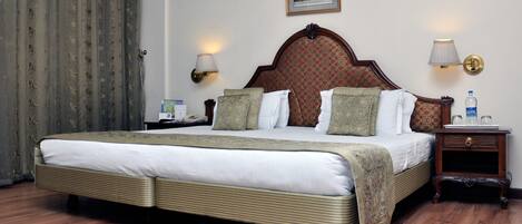 A neatly made bed with a wooden headboard, two bedside tables with lamps, a framed picture on the wall, and a curtain on the left.