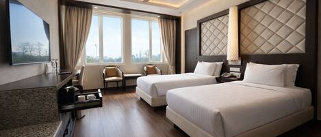 A hotel room with two beds, a desk, a chair, a TV, and a ceiling fan.