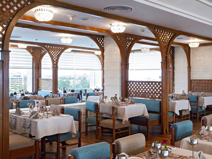 A restaurant with wooden arches, tables set with white tablecloths, and blue upholstered chairs.