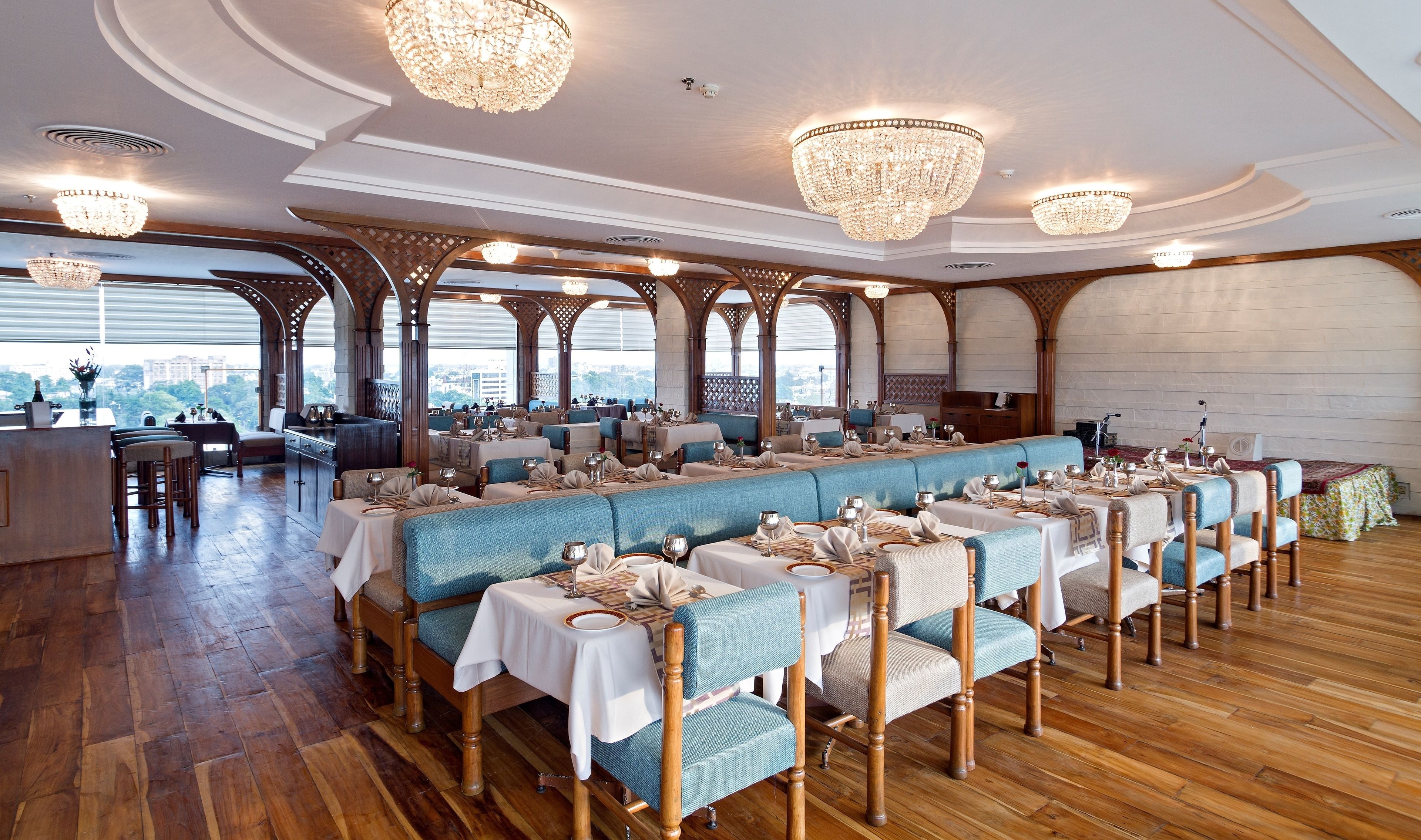 Un restaurante con altos techos de madera, candelabros y una larga zona de comedor con sillas tapizadas en azul y manteles blancos.