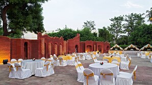 A banquet hall with round tables and chairs, brick walls, and trees in the background.