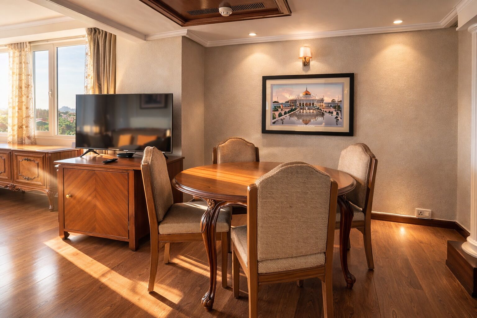 A dining area with a wooden table and chairs, a television on a wooden cabinet, and a framed picture on the wall.
