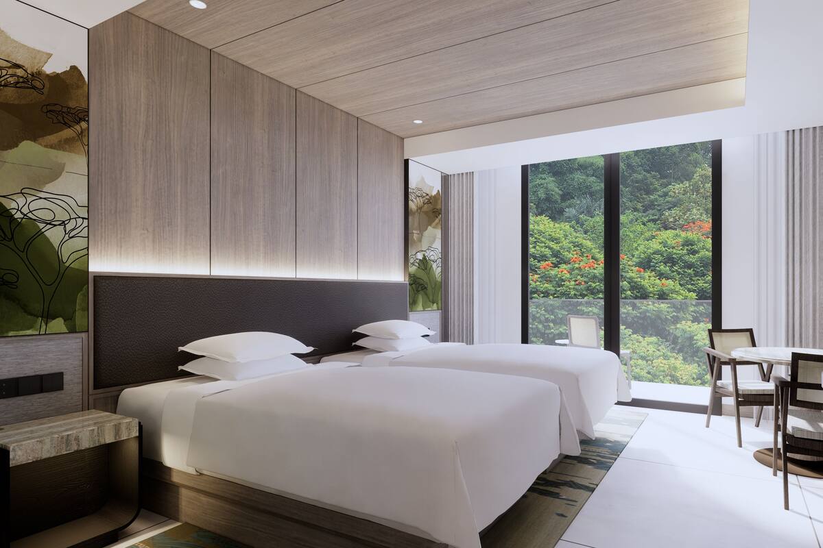 A modern hotel room with two beds, a desk, a chair, and a large window with a view of greenery.