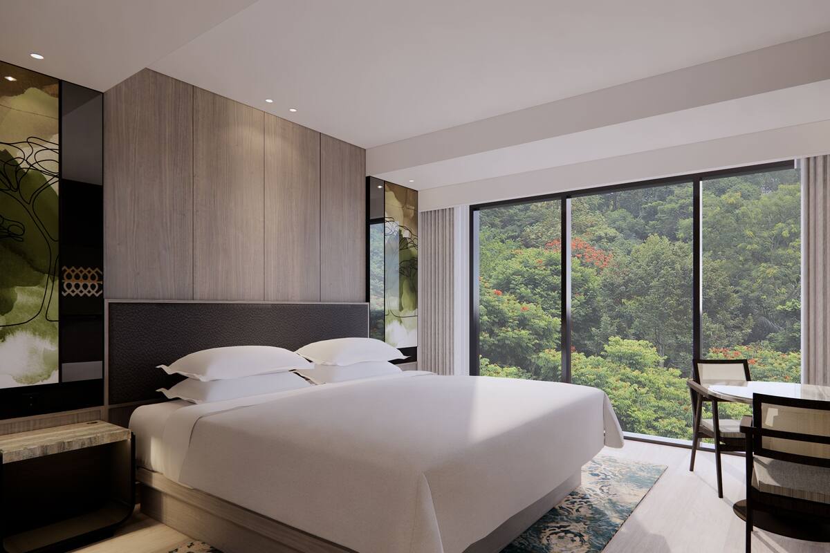 A modern hotel room with a large bed, a desk, and a view of a forest through a large window.