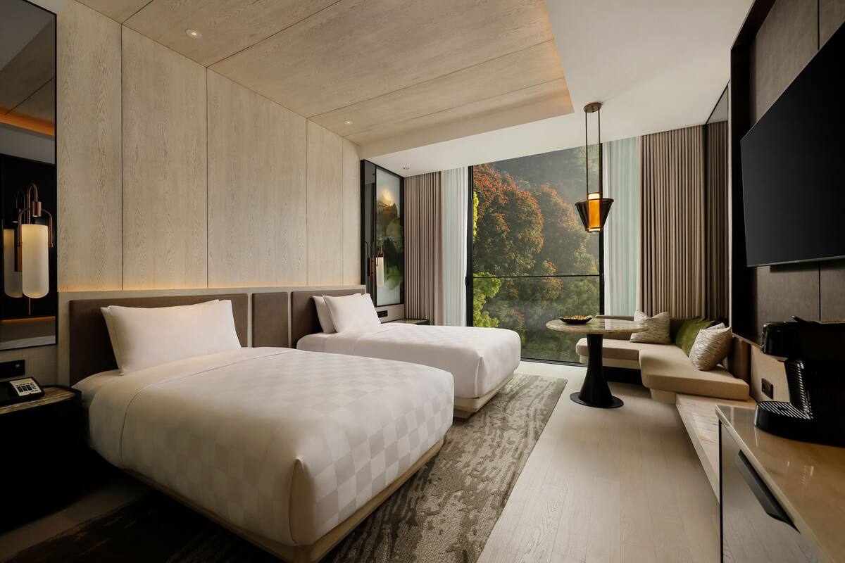A modern hotel room with two beds, a sofa, a TV, and a large window with a view.