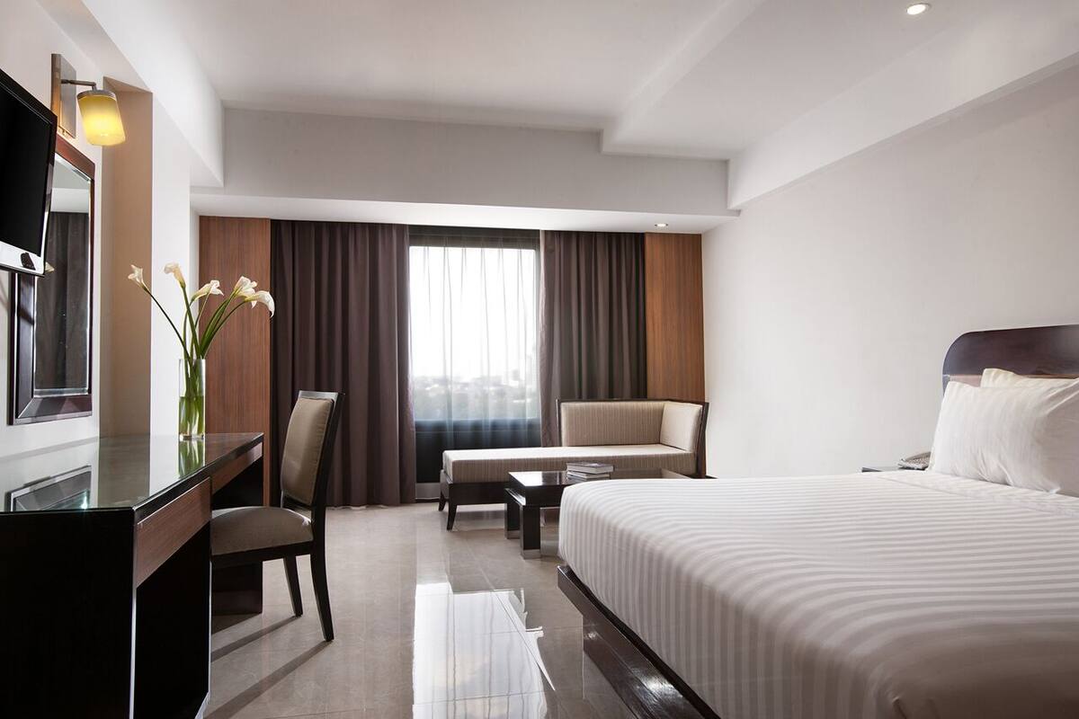 A hotel room with a bed, a sofa, a desk, and a TV.