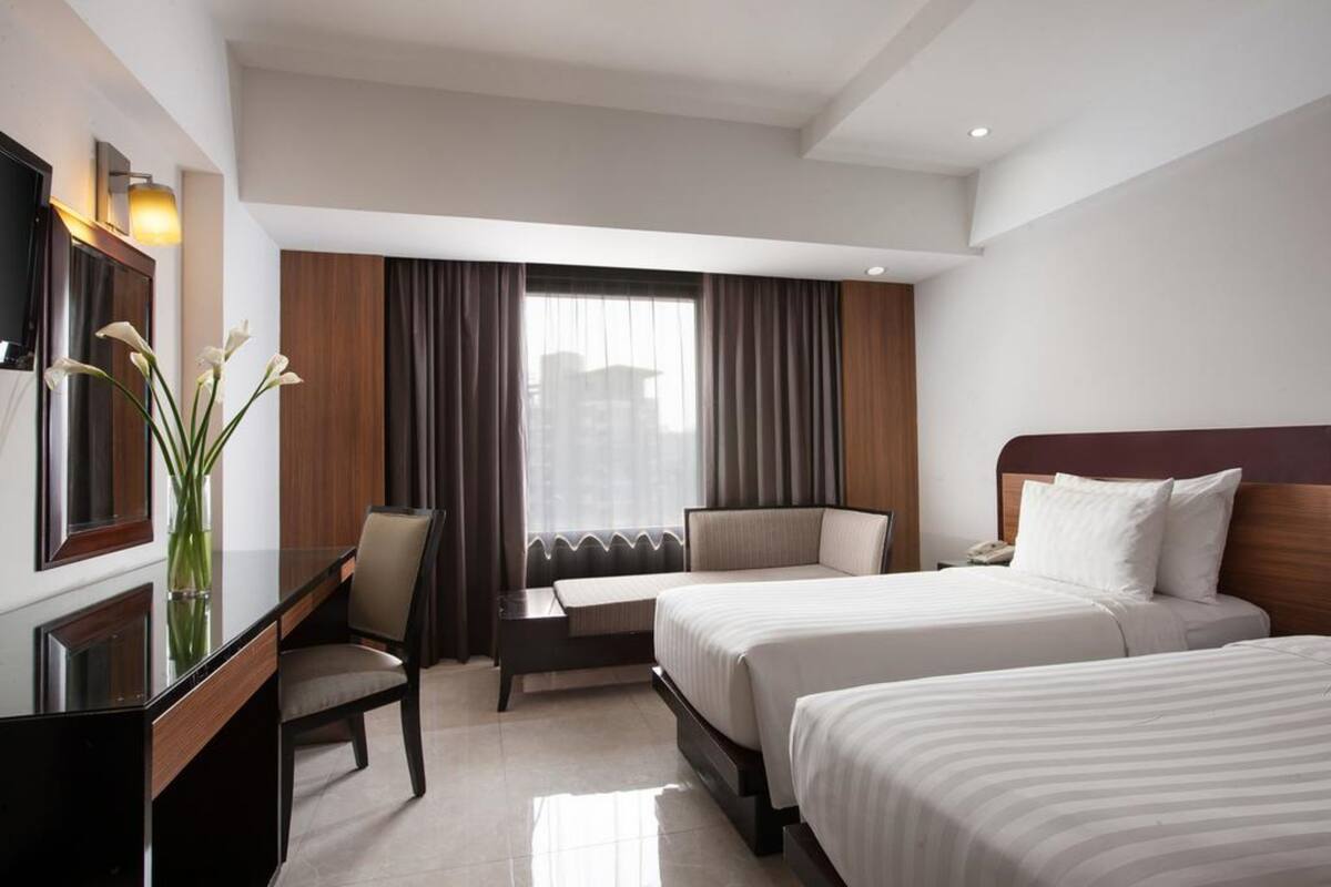 A hotel room with two beds, a desk, a chair, and a large window with curtains.