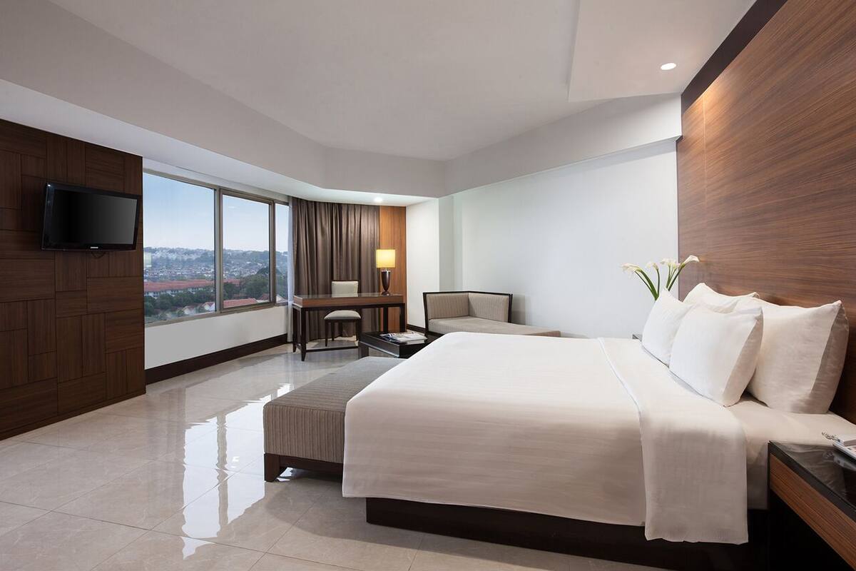 A modern hotel room with a large bed, a desk, a chair, and a TV.