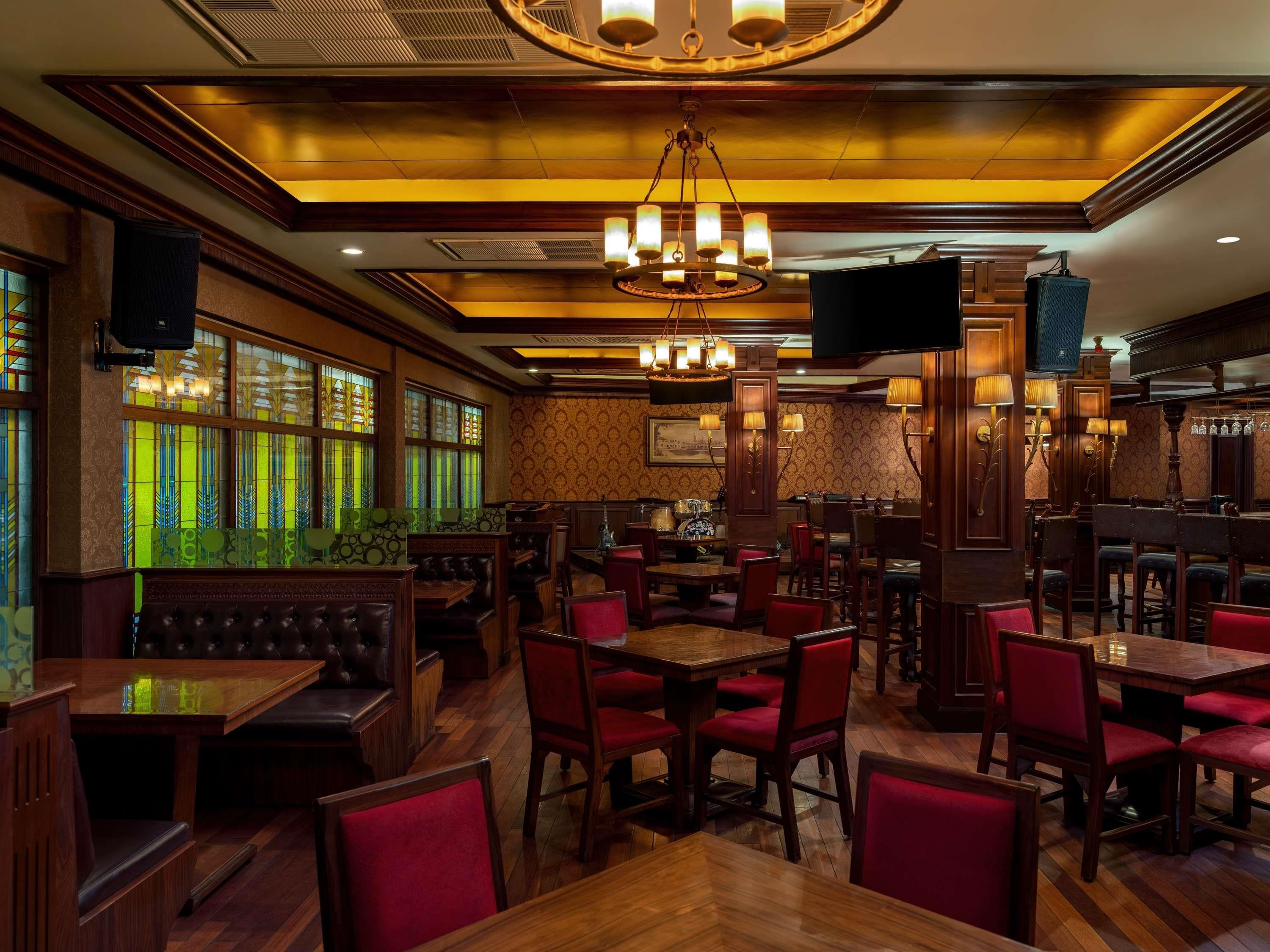 A restaurant with wooden tables and red upholstered chairs, a chandelier, and stained glass windows.