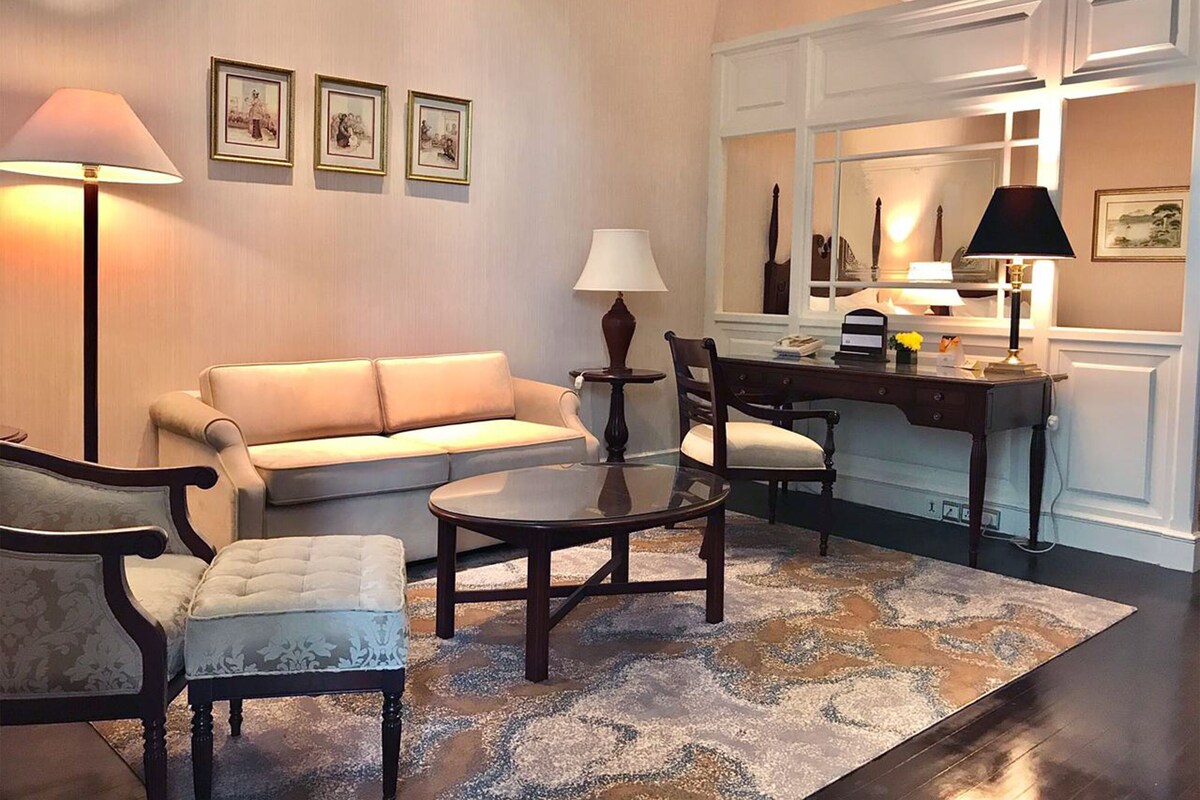Un salon comprenant un canapé, deux fauteuils, une table basse, un bureau avec une lampe et un grand miroir.