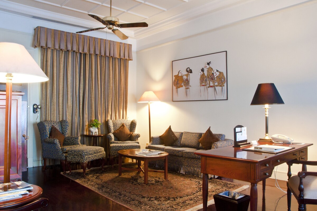 Un salon avec un ventilateur de plafond, un canapé, deux fauteuils, une table basse et un bureau avec une lampe.