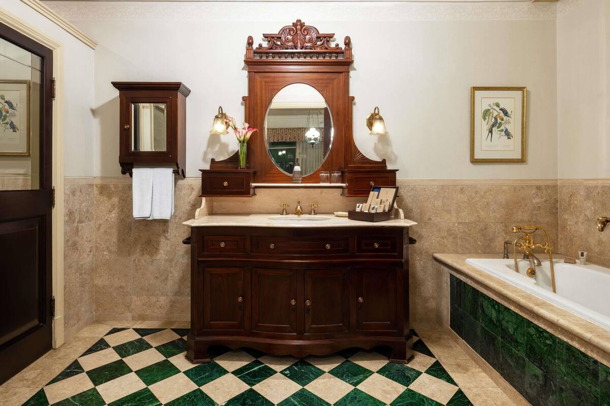 Ein Badezimmer mit Schachbrettboden, einem großen Spiegel, einem Waschtisch und einer Badewanne.