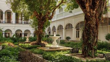 A courtyard with a fountain, large trees, and a building with arched windows and balconies.