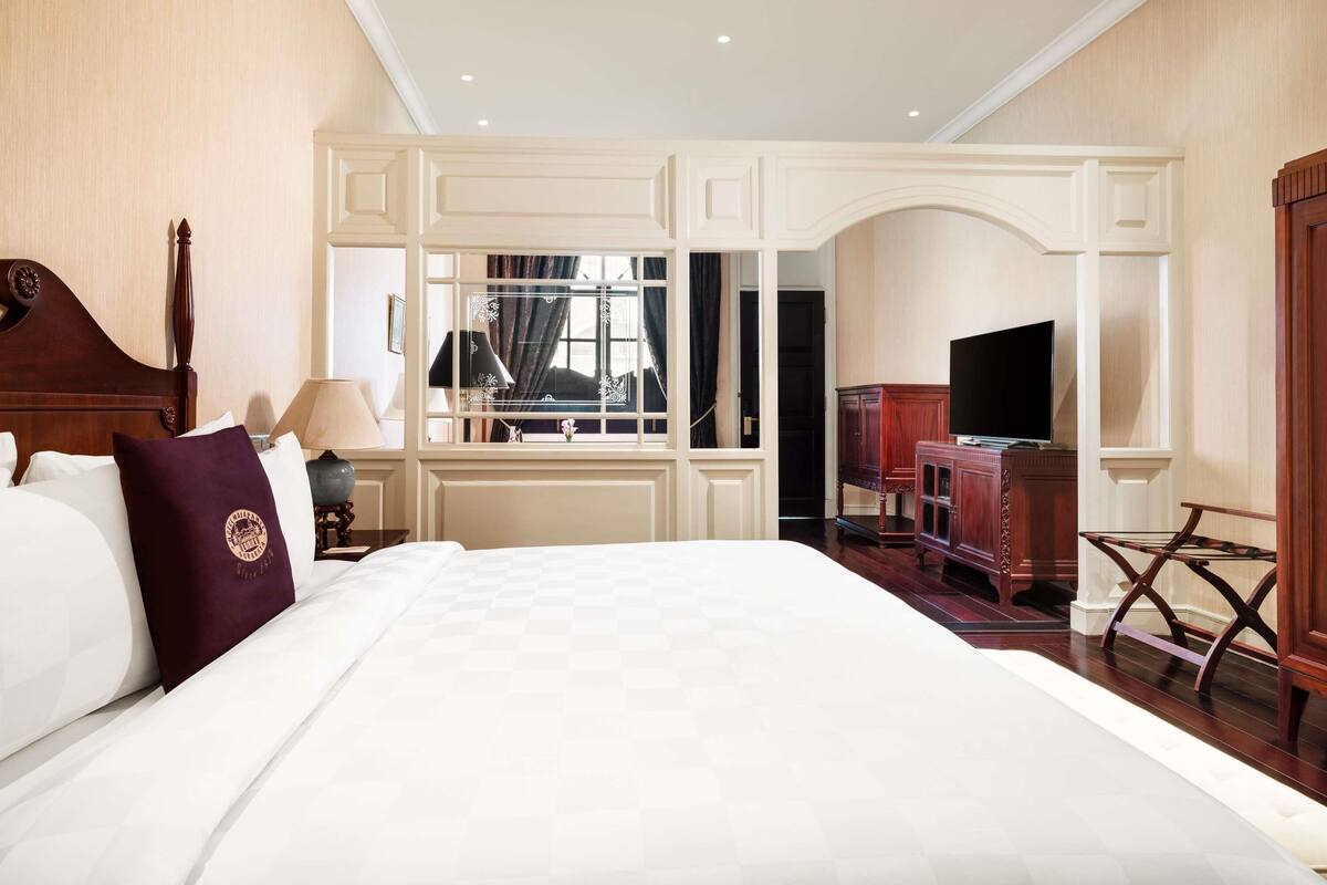 Ein Hotelzimmer mit einem großen Bett, einem Fernseher, einem Schreibtisch und einem Spiegel.