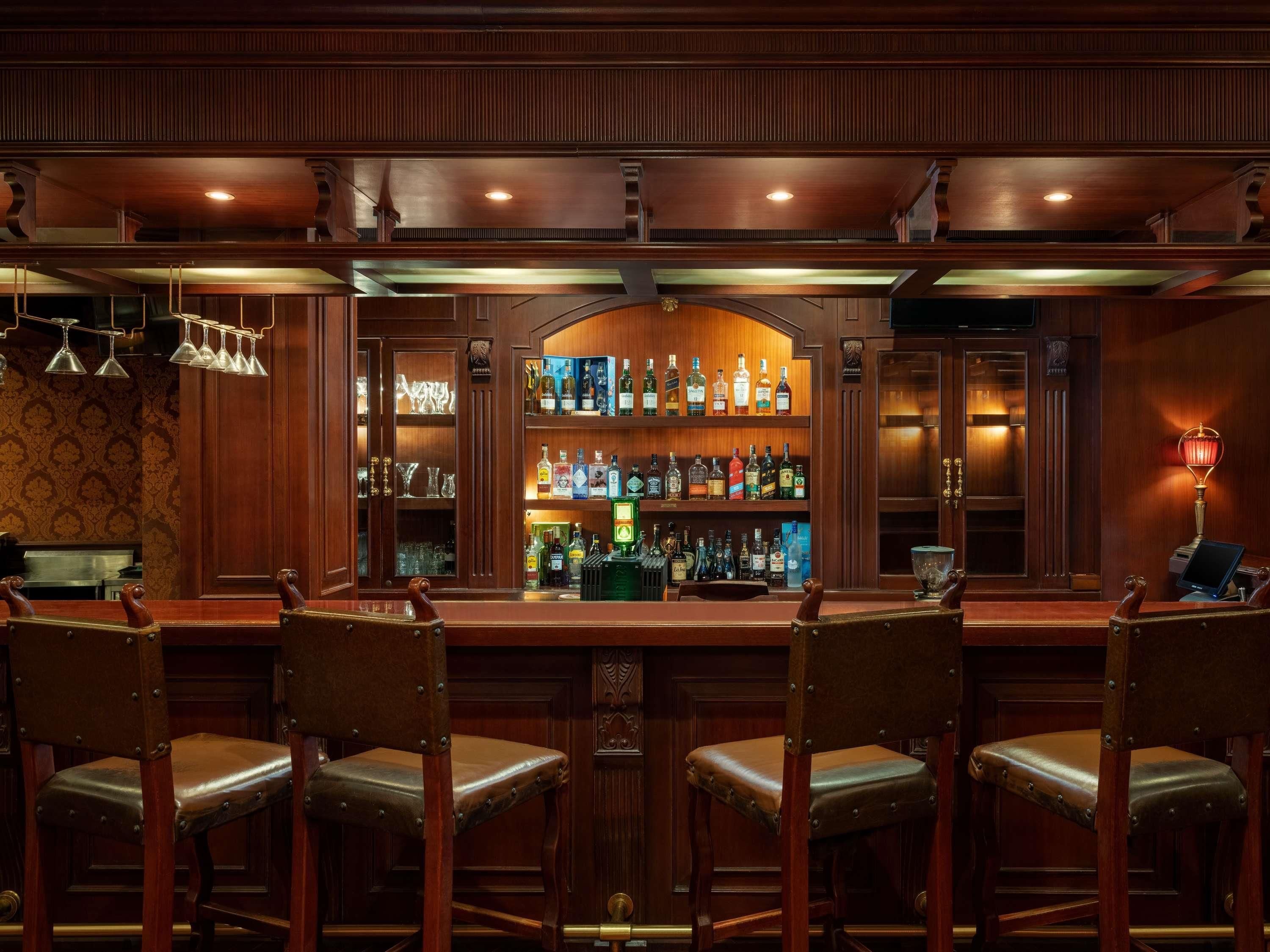Een bar met houten lambrisering, een drankendisplay en leren barstoelen.