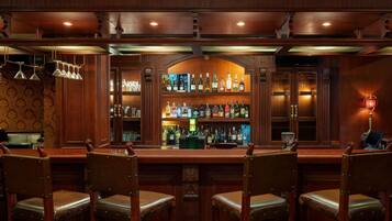 Een bar met houten lambrisering, een drankendisplay en leren barstoelen.