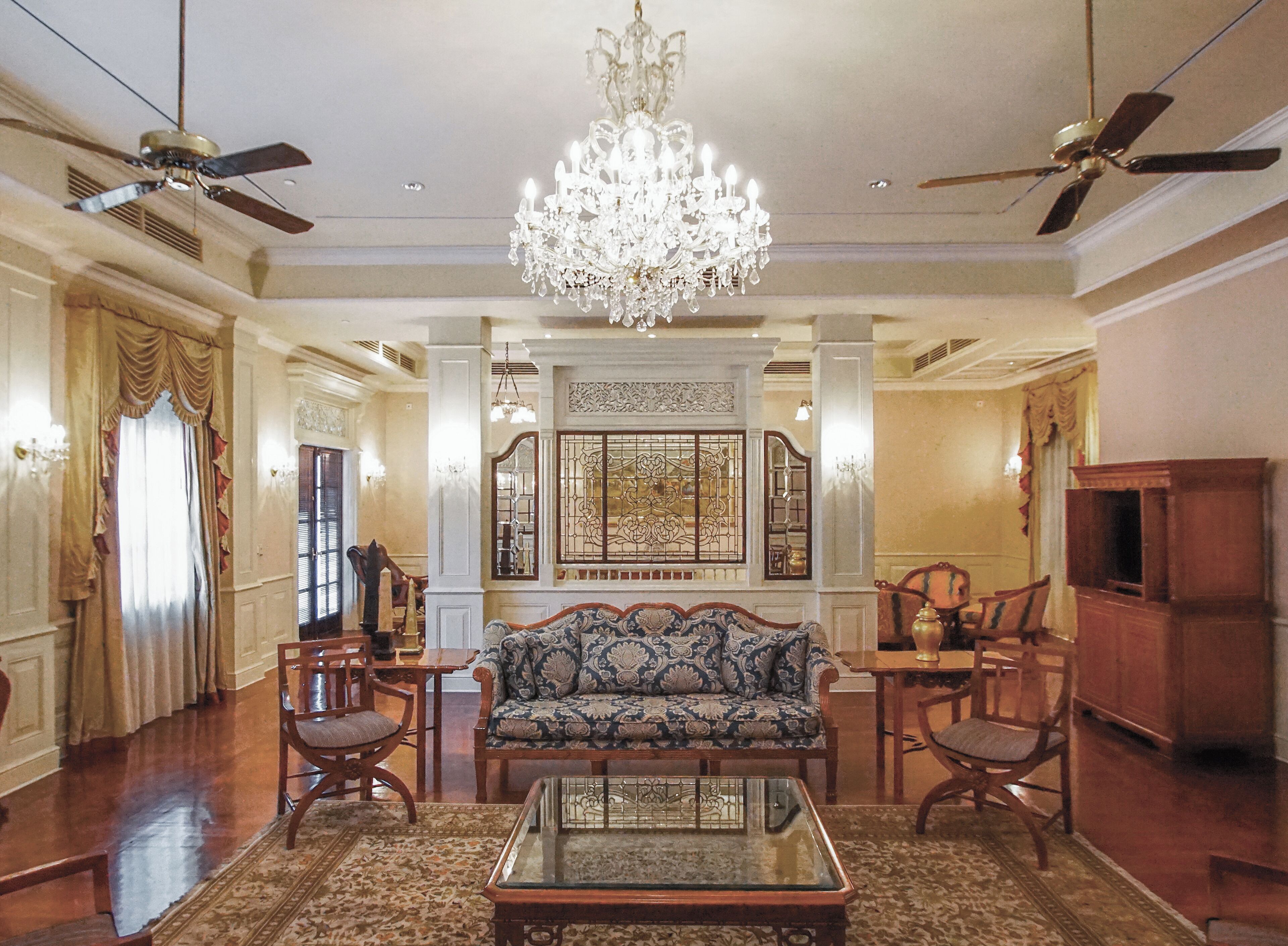 A spacious living room with a chandelier, a sofa, chairs, a coffee table, and a television.