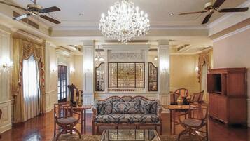 A spacious living room with a chandelier, a sofa, chairs, a coffee table, and a television.
