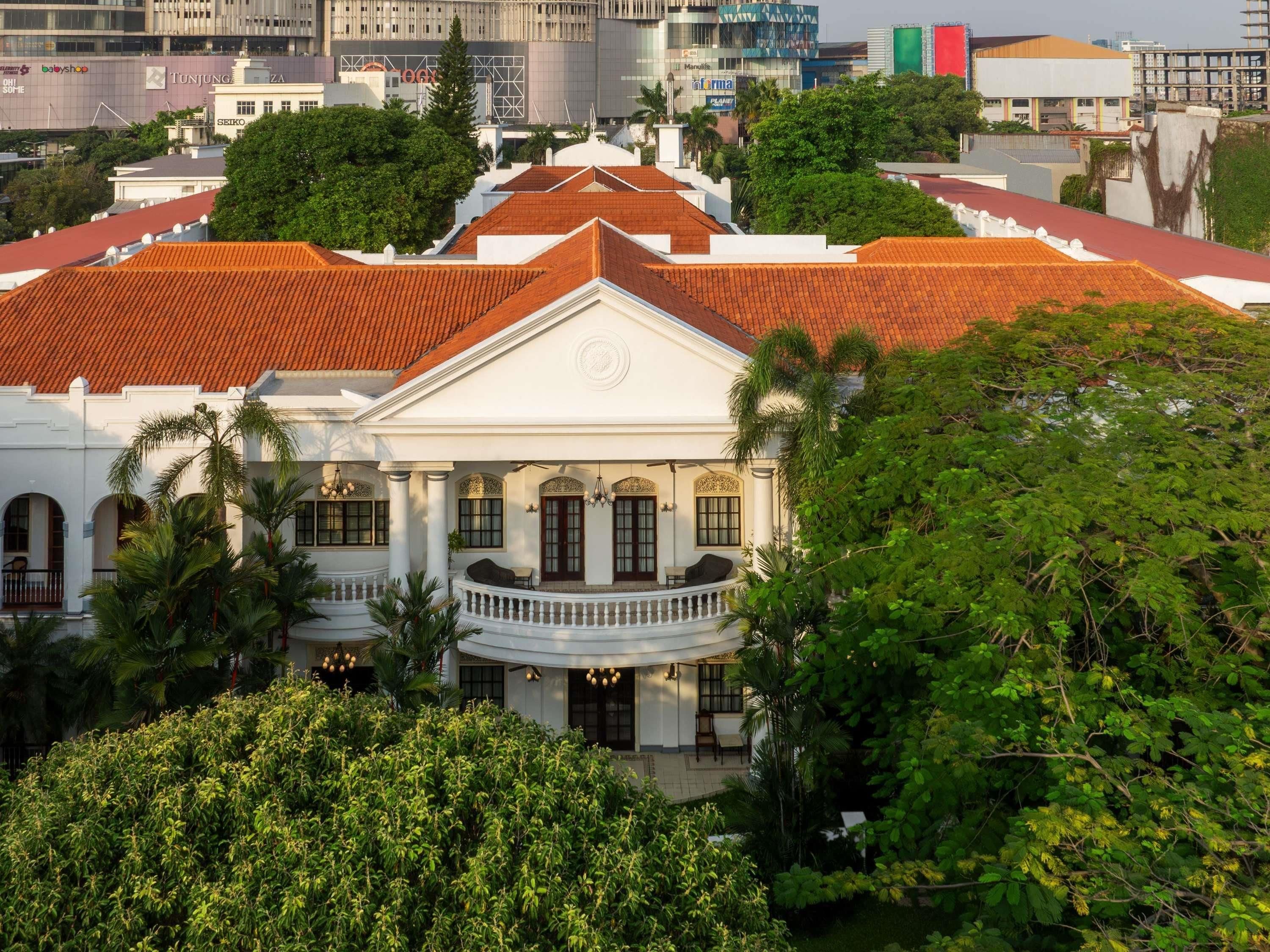 A colonial-style building with a central balcony, surrounded by lush greenery.