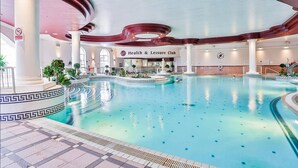 An indoor swimming pool with a Health & Leisure Club sign, surrounded by columns and potted plants.