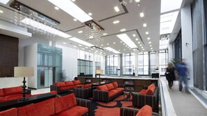 Un hall d’entrée moderne avec des canapés rouges, une table basse centrale et un ascenseur en verre.