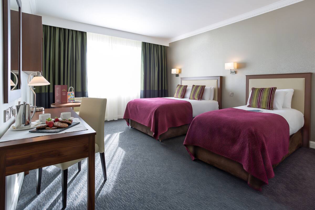 Habitación de hotel con dos camas, un escritorio con una computadora portátil, una silla y una ventana con cortinas.