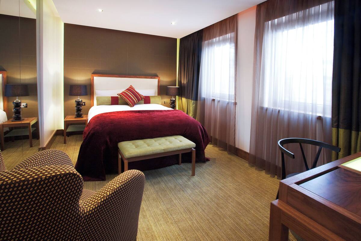 Una habitación de hotel con una cama grande, un banco, una mesa de comedor y dos sillas.